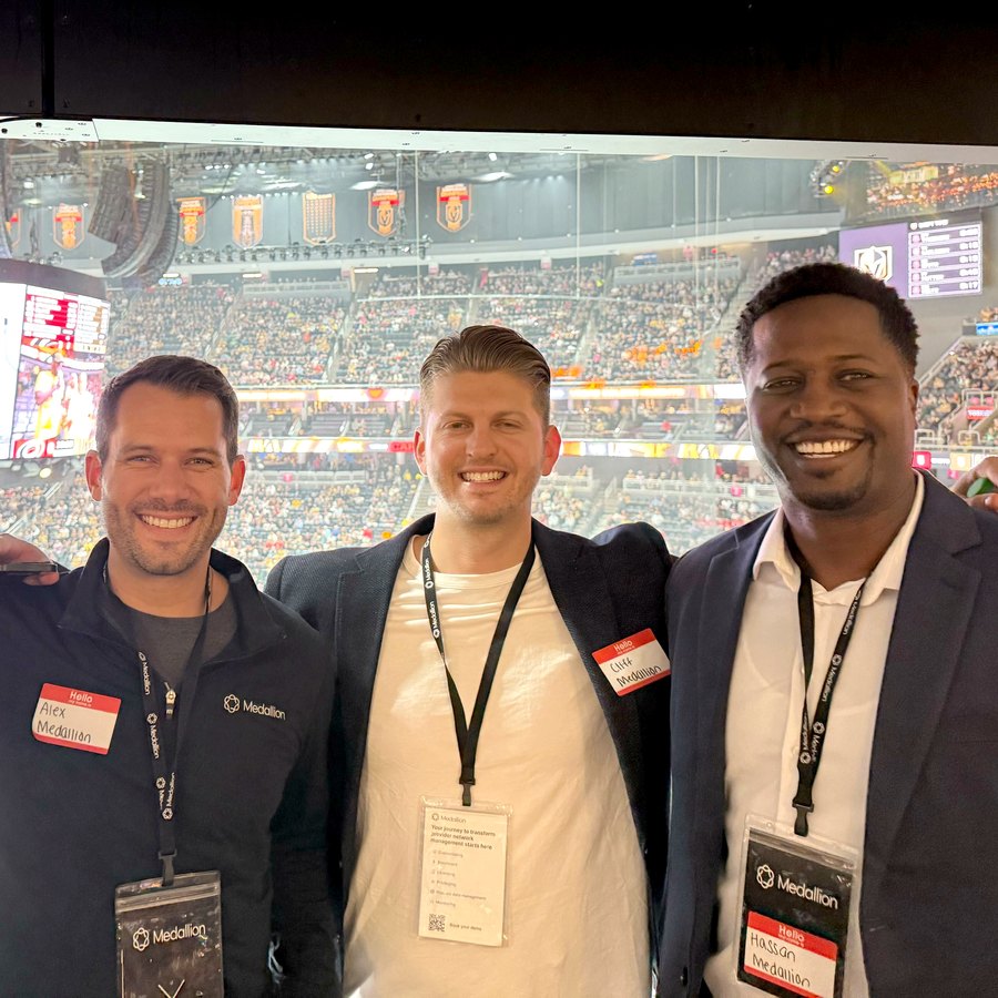 Three Medallion team members in the suite at T-Mobile Arena, the crowd and rink behind them